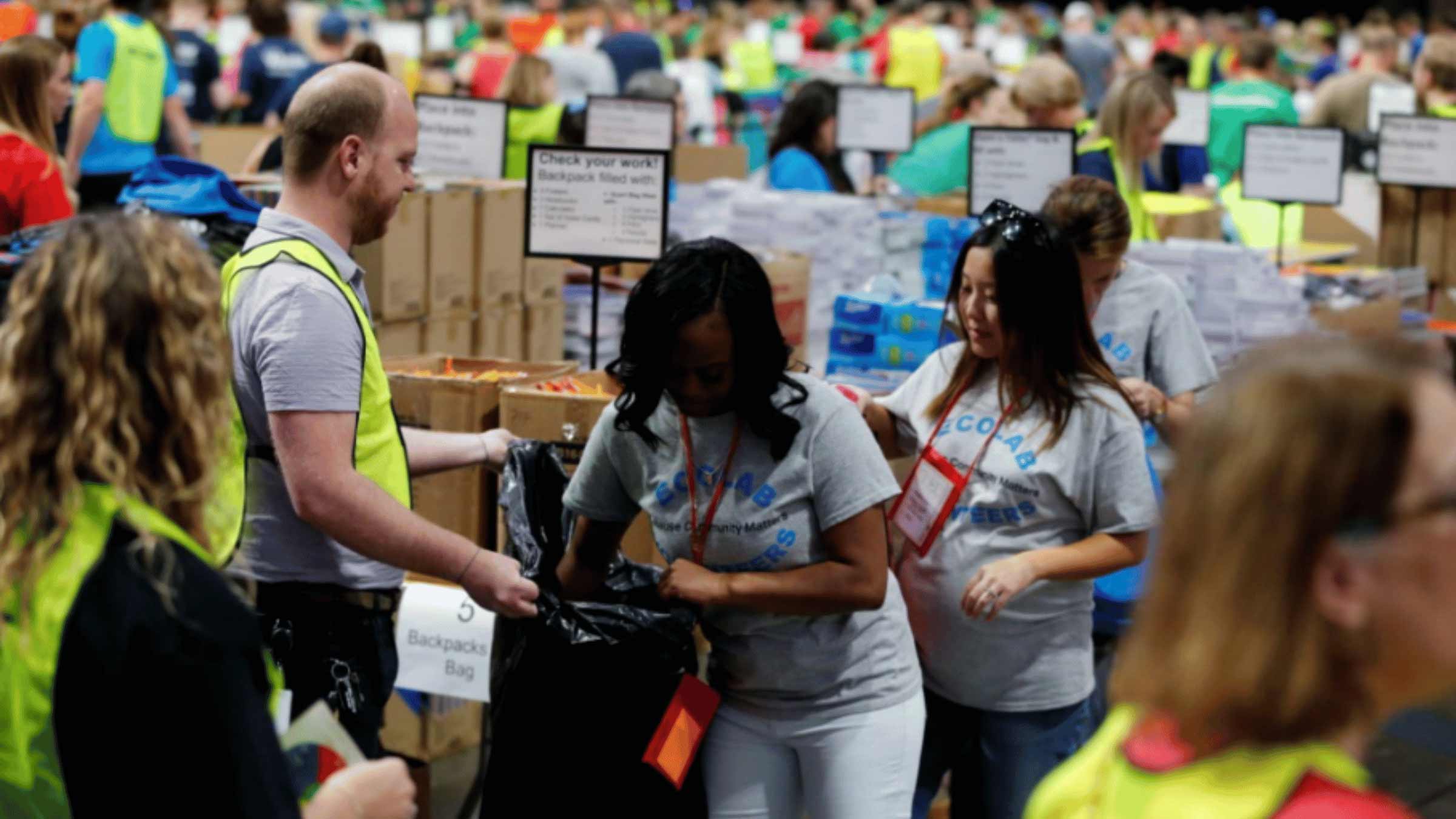 A volunteer is packing a backpack surrounded by other volunteers