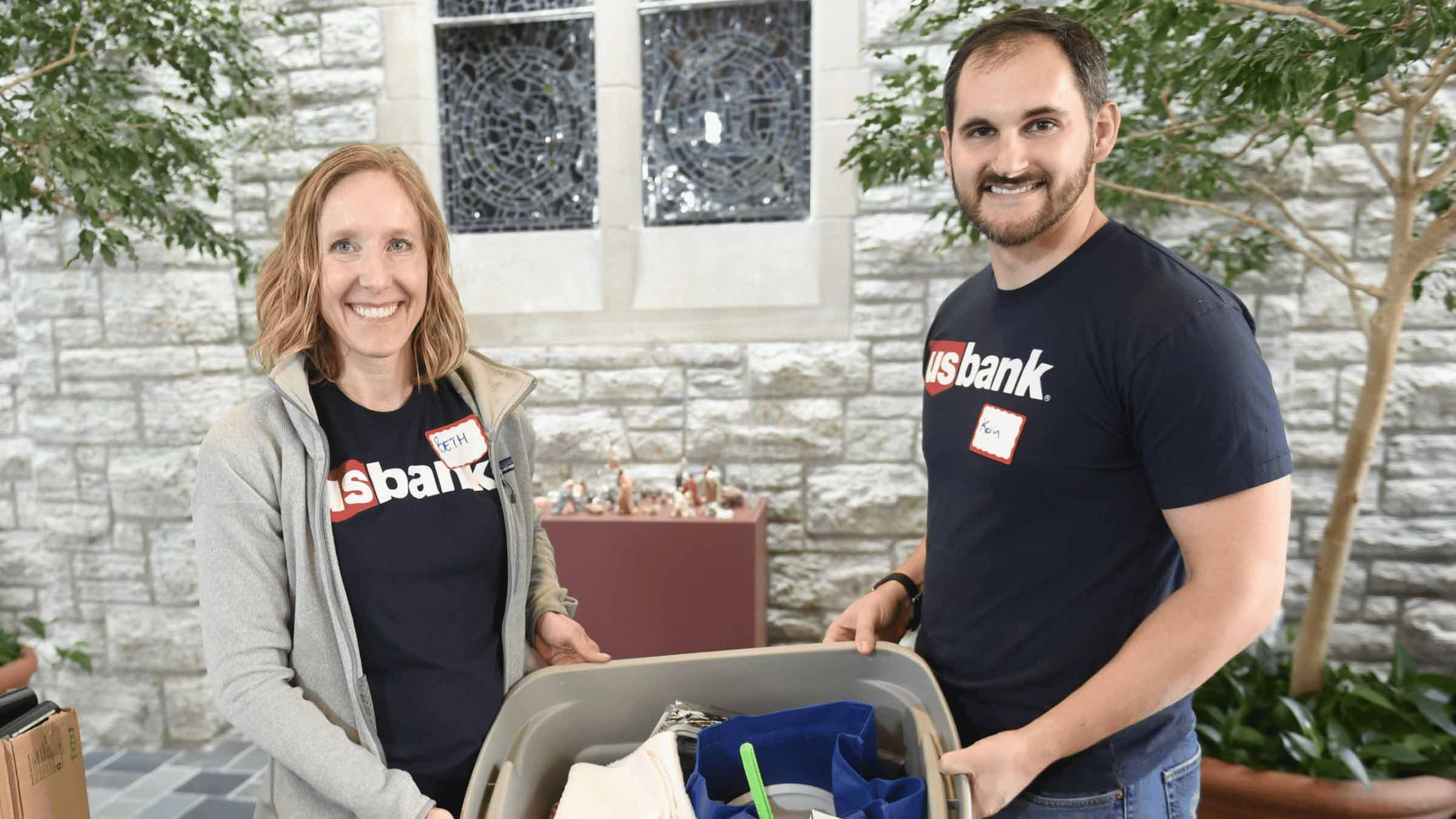 Two volunteers from US Bank hold up a bin filled with supplies