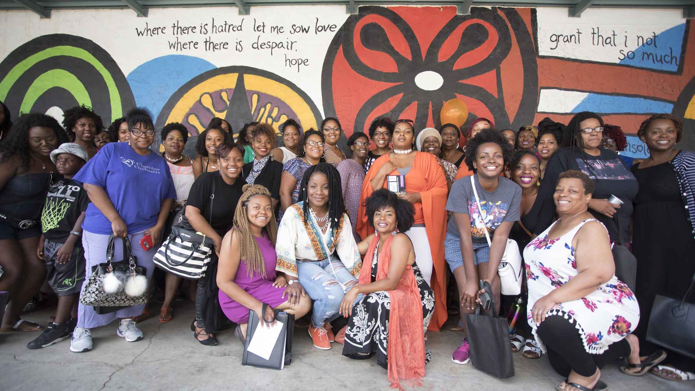 A group of Black women stand in front of a mural