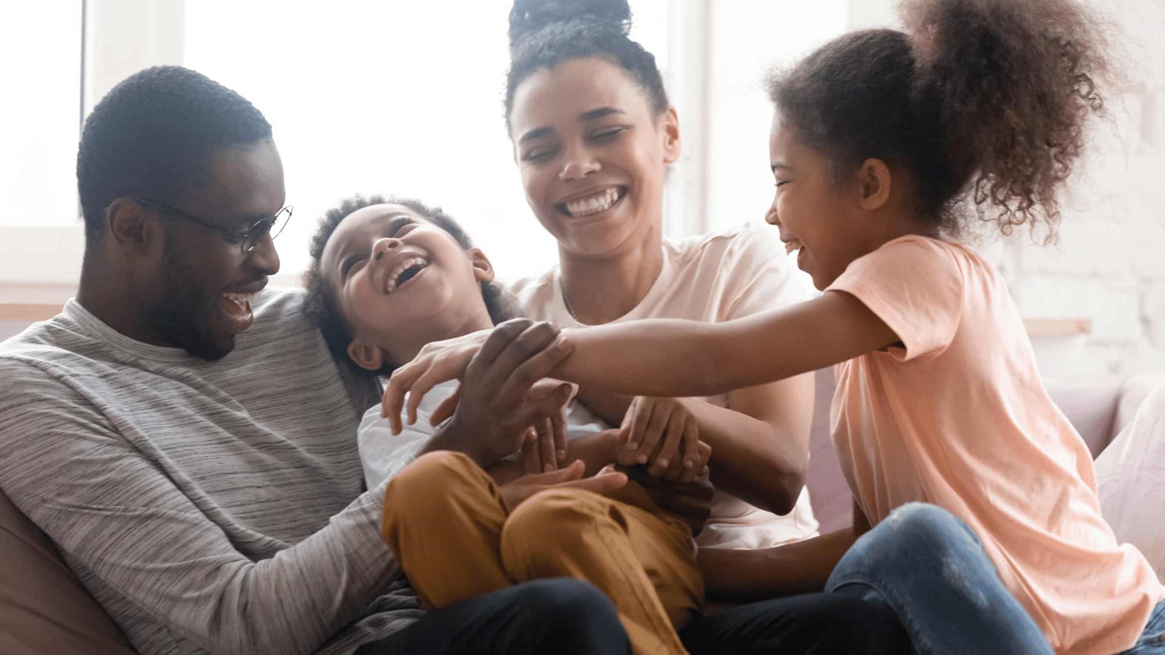 A family of four sits together on a couch laughing