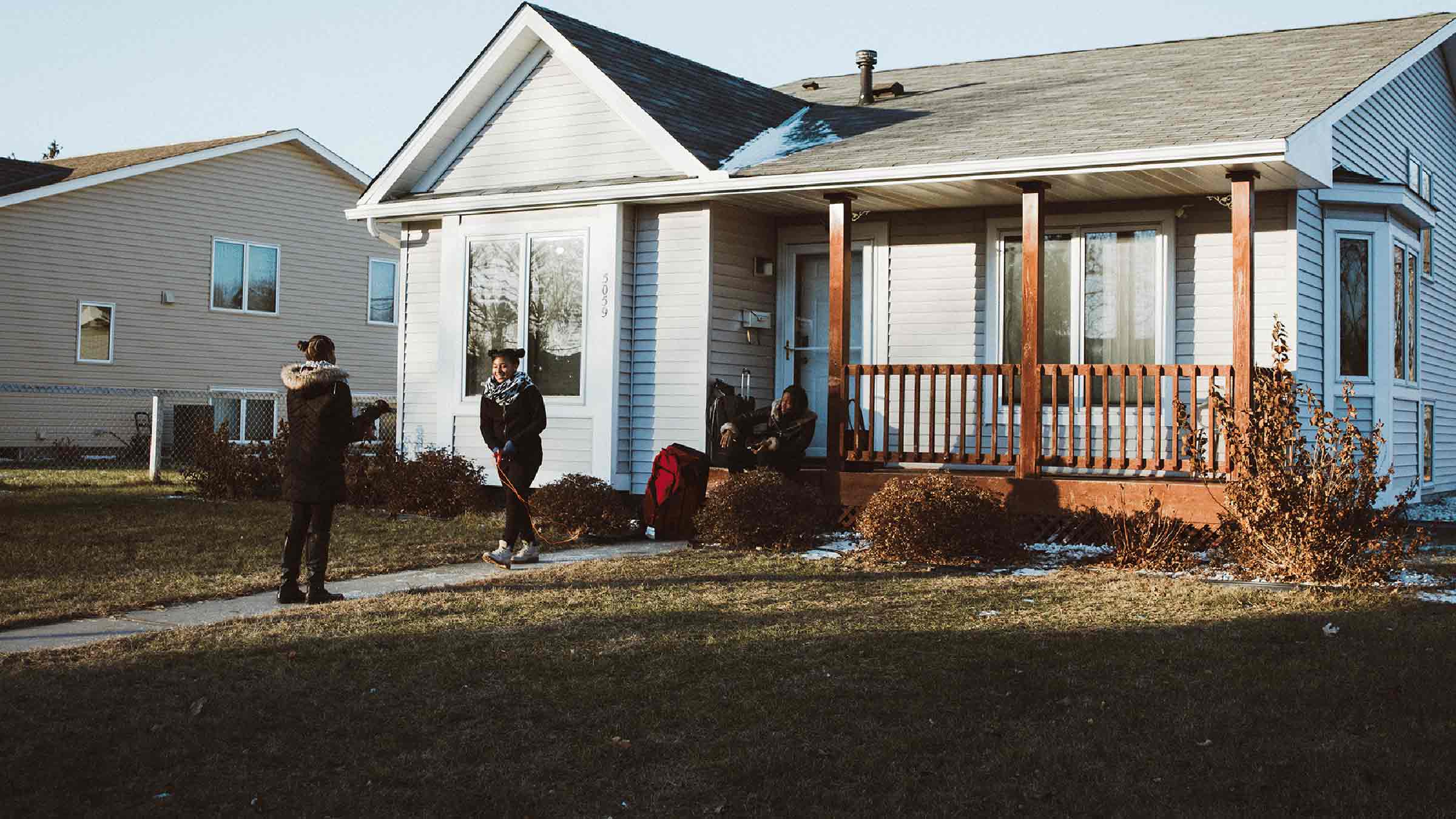 A parent with her two children stand outside of their house during the spring time