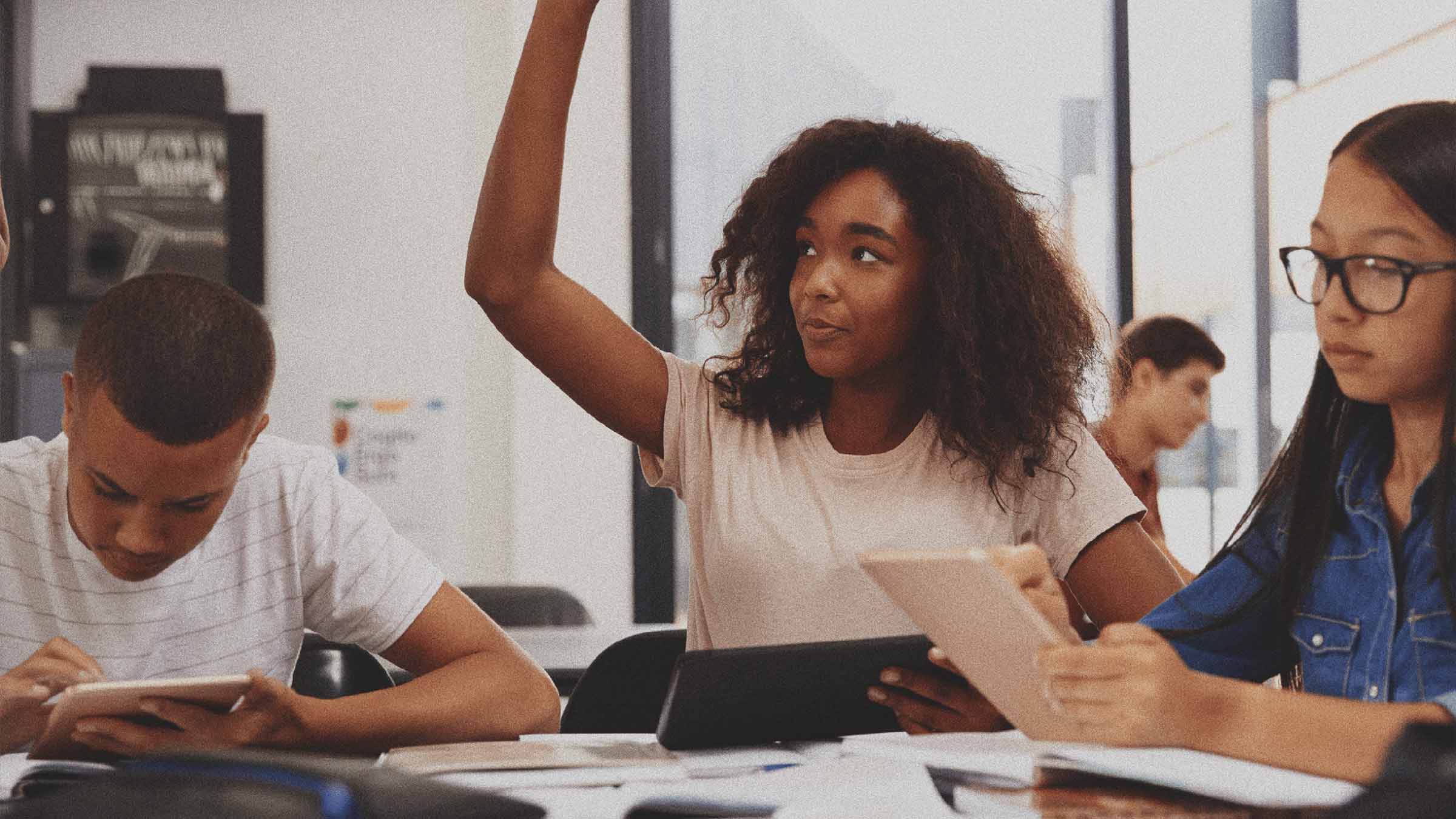 A group of students are sitting together and the middle student is raising her hand