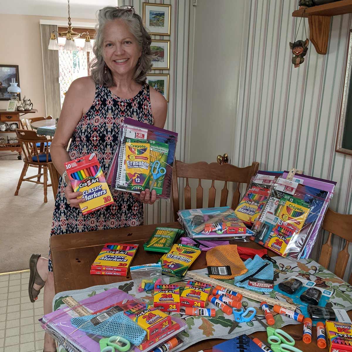 A volunteer stands in her dining room with several school packs that will be donated to Action Day