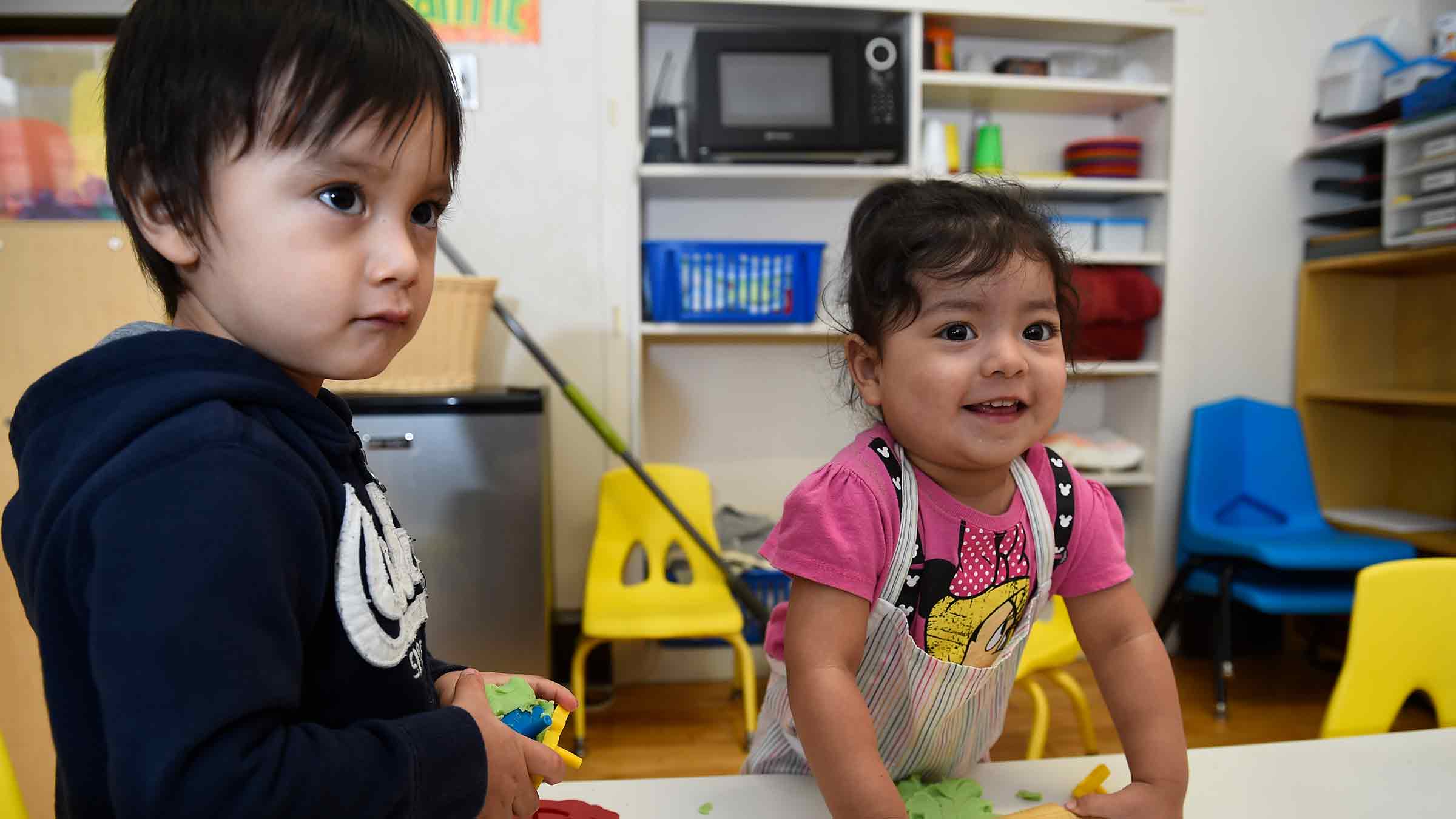 Two young children play with PlayDoh at their preschool