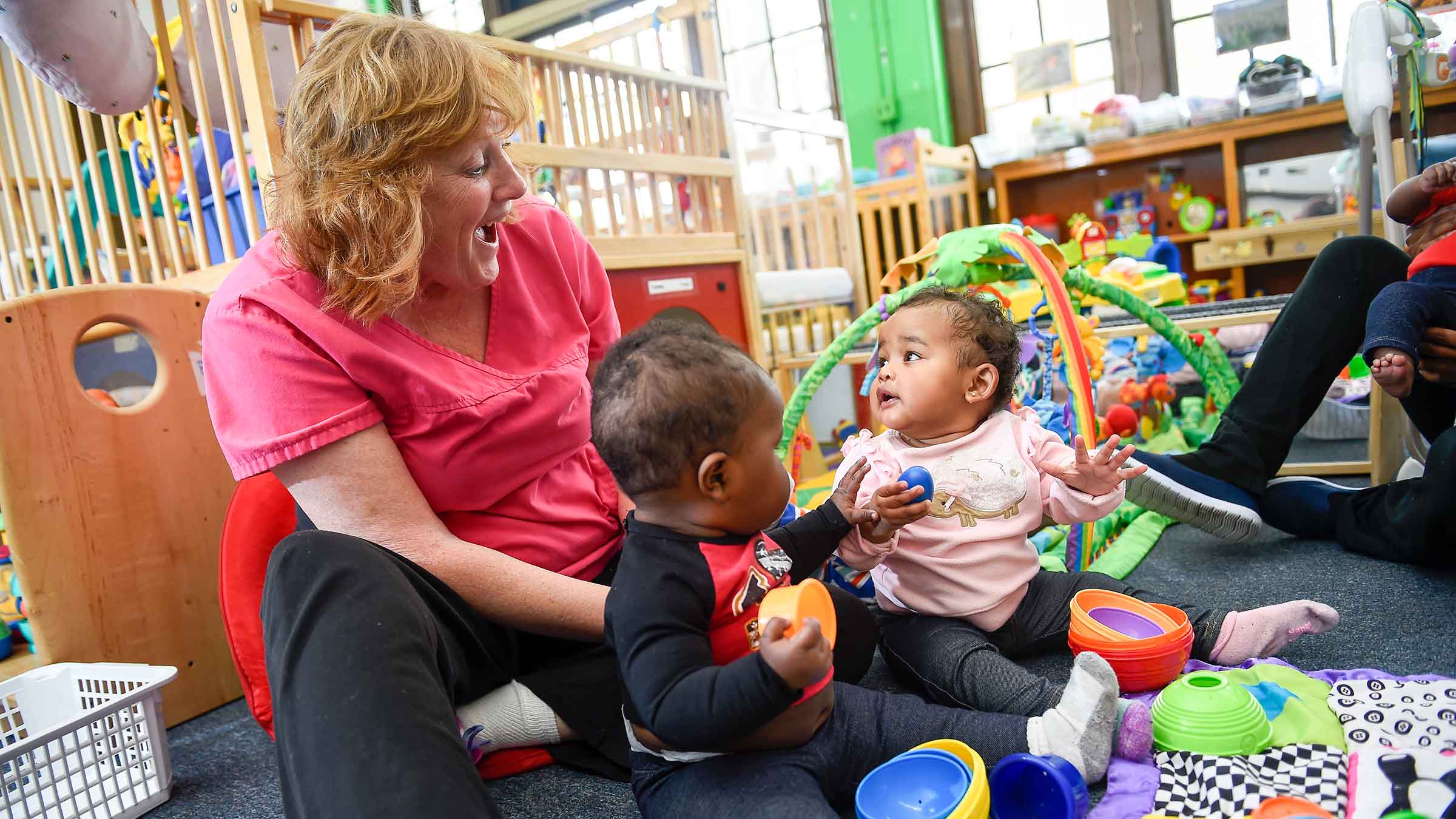 An early childhood education teacher is playing with two babies