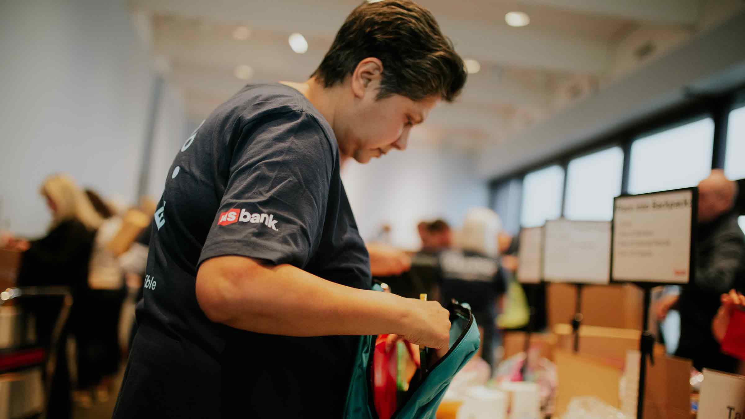 A volunteer with US Bank is packing a backpack at Action Day