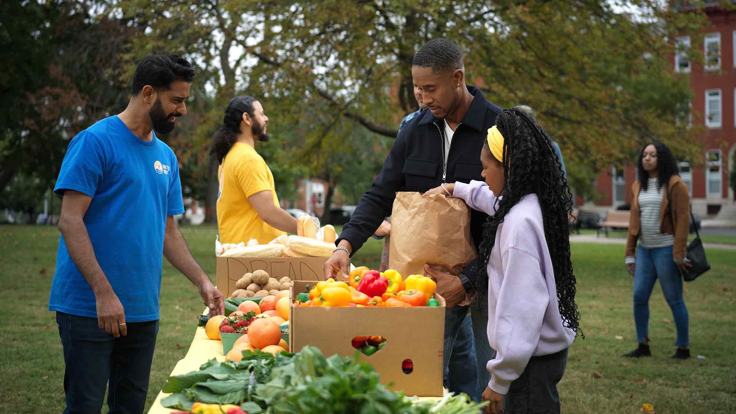 Community members select fresh produce at an outdoor food distribution table.