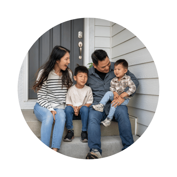 A young family sitting on the steps of their home, smiling and laughing.