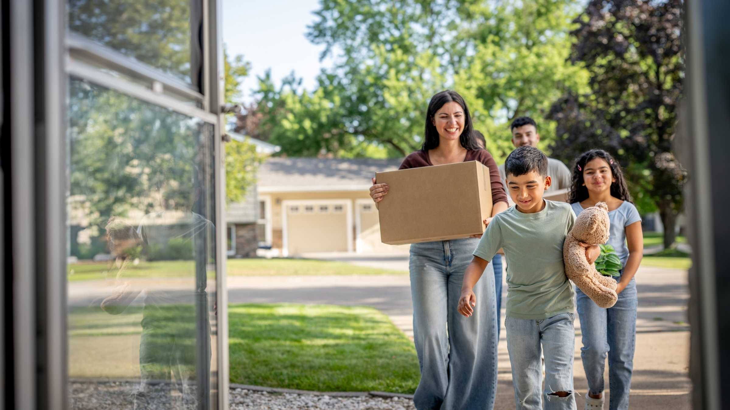 A family cheerfully entering their new house with moving boxes.